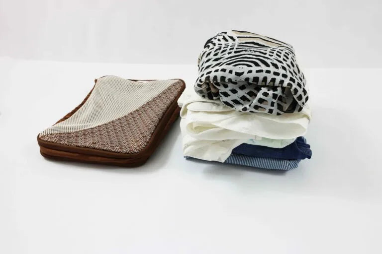 Folded clothes stacked next to a brown Caveri compression packing cube on a white surface