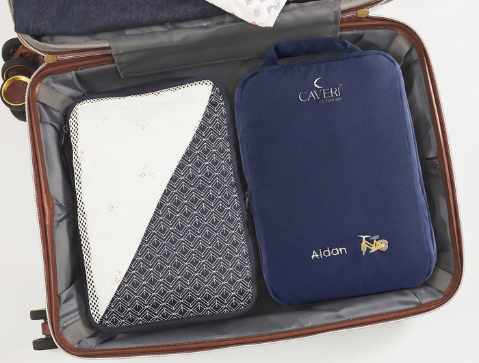 An open brown suitcase showing packed travel organizers inside, including a navy blue Caveri compression packing cube with emrboidered personalised name Aidan and bicycle motif. 