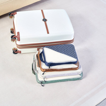 Caveri compression packing cubes in navy, tan and sage stacked beside a white hardcase suitcase