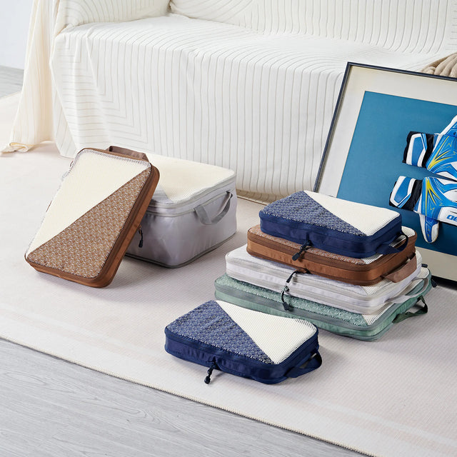 Caveri packing cubes set in navy, tan, grey and sage arranged on bedroom floor in multiple sizes