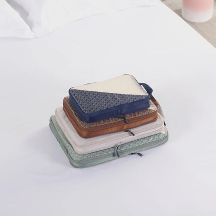 Caveri packing cubes set stacked on bed in navy, tan, sand and sage green with geometric print