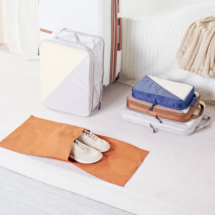 Caveri packing cubes set with shoe bag in tan, blue and white beside open suitcase