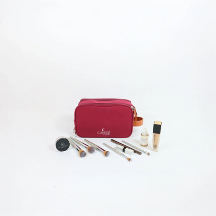 Caveri toiletry bag in berry red with tan handle, shown with makeup brushes, foundation and skincare