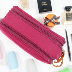 Caveri toiletry bag in fuchsia with three zip compartments and tan leather pull, styled with perfume and cosmetics