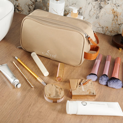 Caveri toiletry bag in sand beige with tan leather handle, styled on bathroom vanity with makeup and skincare