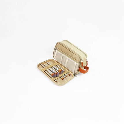 Caveri toiletry bag in sand open to show makeup brush holder and mesh pocket with orange leather handle