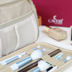 Caveri toiletry bag open in sand showing brush roll and mesh pocket, with berry red bag in background