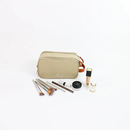 Caveri toiletry bag in sand with tan leather handle, shown with makeup brushes and skincare products