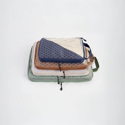 Caveri Wanderlust packing cubes stacked in navy, tan, and sage green with geometric print and mesh panels
