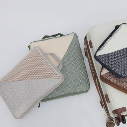 Caveri Wanderlust packing cubes in sage, stone and navy with mesh panels beside a white hardcase suitcase