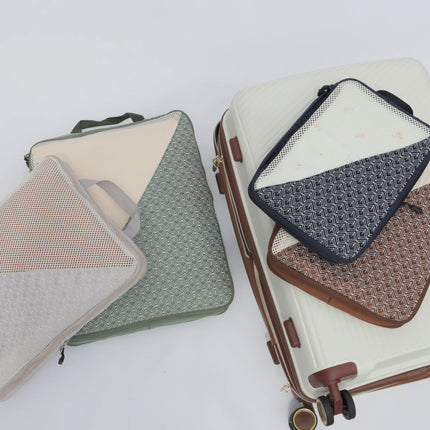 Caveri Wanderlust packing cubes in sage, sand, navy and brown with mesh panels beside a white suitcase