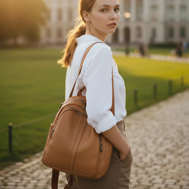 Woman wearing Caveri Zea day bag in tan leather as a backpack on a cobblestone path
