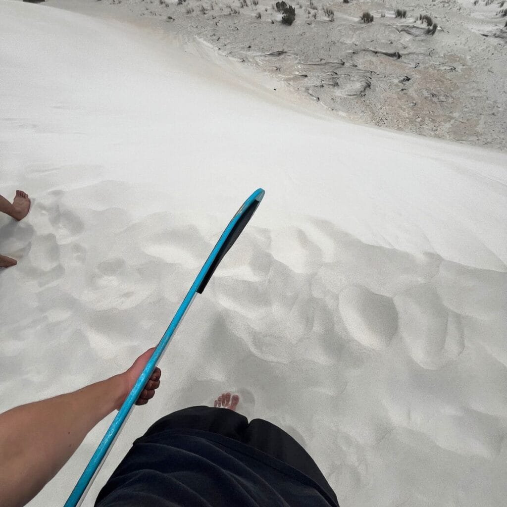 A person sandboarding down a steep dune at Lancelin, kicking up a trail of golden sand