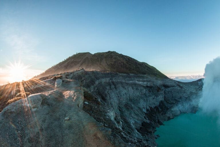 The turquoise crater lake of Kawah Ijen illuminated by sunrise, surrounded by volcanic cliffs and sulphuric smoke