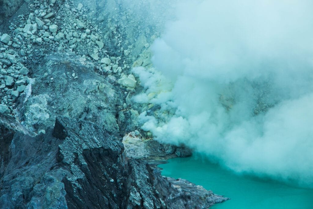 The turquoise crater lake of Kawah Ijen illuminated by sunrise, surrounded by volcanic cliffs and sulphuric smoke