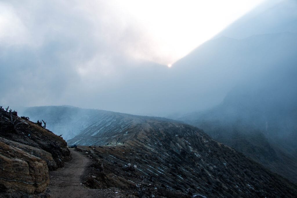 The turquoise crater lake of Kawah Ijen illuminated by sunrise, surrounded by volcanic cliffs and sulphuric smoke